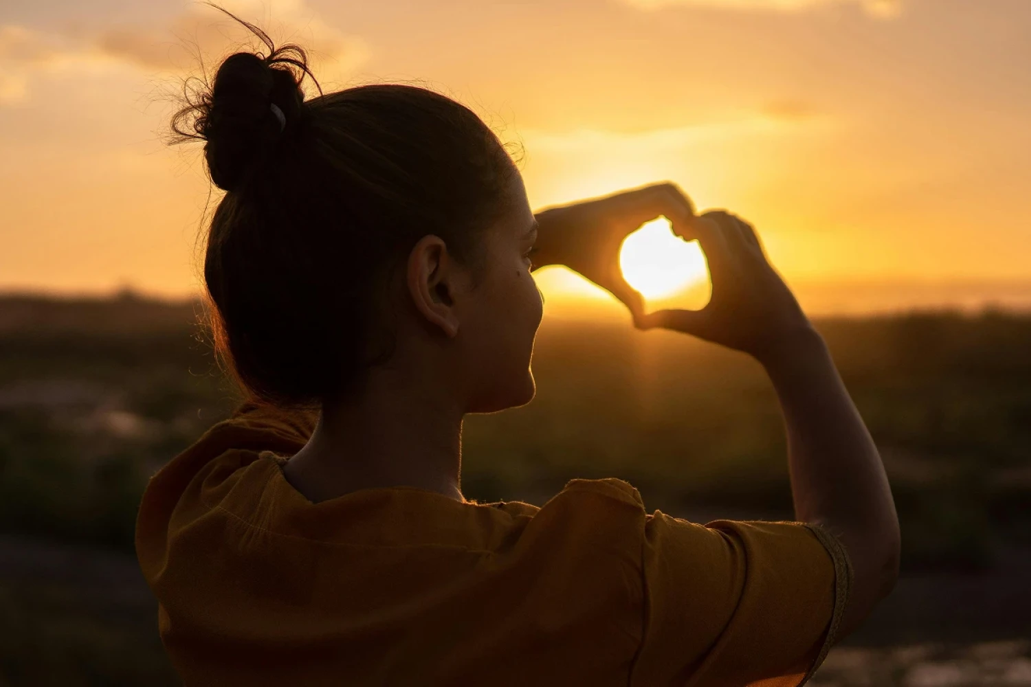 Frau zeigt Herz mit Händen vor Sonnenuntergang